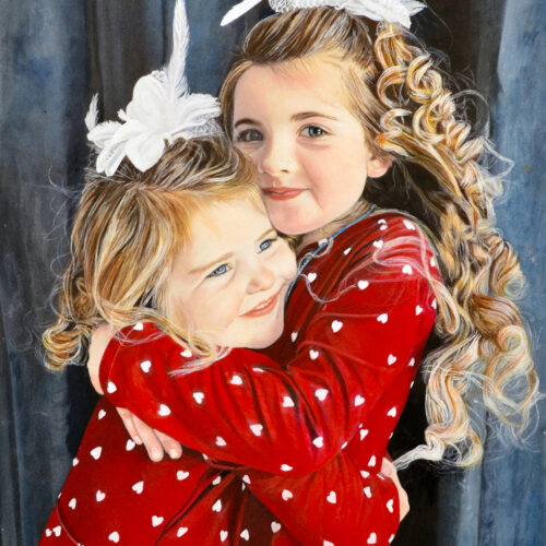 two young girls with long, curly blonde hair wearing red dresses with white hearts hug and smile, each with a large white bow in their hair, standing in front of a dark blue background.