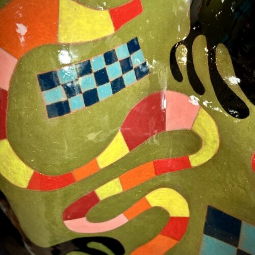 a close up of a glossy, abstract sculpture featuring colorful geometric and wavy patterns in red, yellow, blue, black, and green, with a checkerboard design and curving lines on its surface.