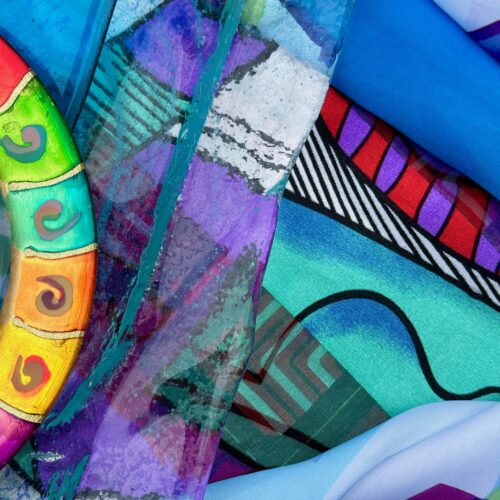 colorful abstract artwork featuring swirling blue, purple, green, and red patterns with bold geometric shapes, wavy lines, and a painted circular object with yellow, orange, and green sections on the left side.
