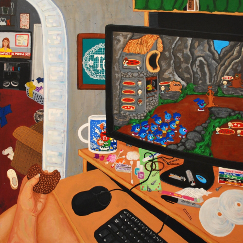 A person eating a chocolate wafer sits at a desk cluttered with snacks and cables, playing a retro computer game featuring blue creatures. A messy room is visible in the background.