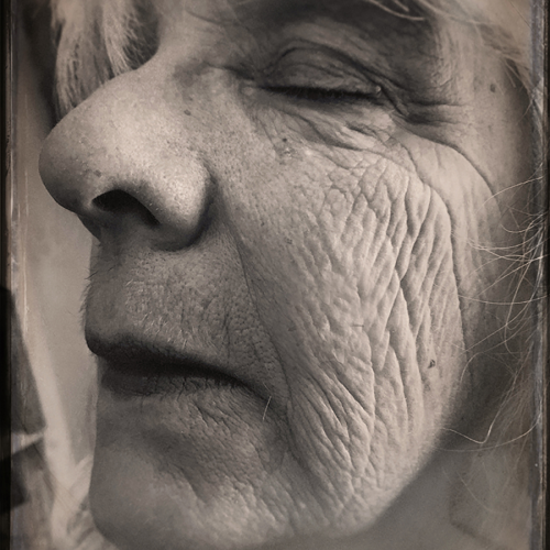 Close-up profile of an older woman with her eyes closed, captured in a sepia-toned, vintage-style photograph.