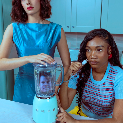 Two women stand in a kitchen with a light blue Smeg blender that has a man’s face visible inside the glass jar.