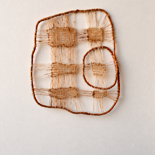 Wall-mounted fiber art consisting of two organic-shaped twig frames interconnected by woven tan string.