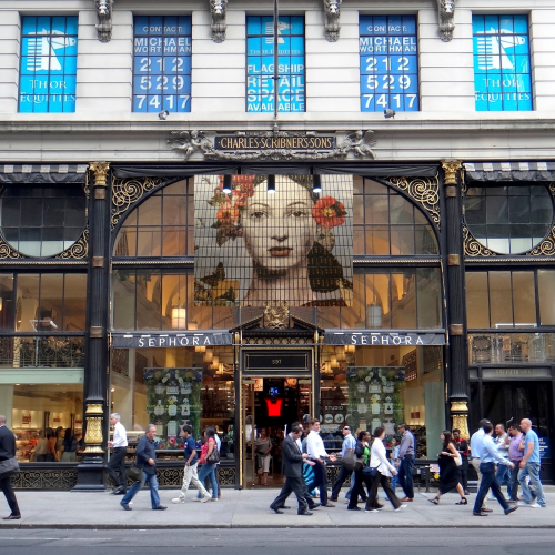 People walk past a Sephora store in an ornate building with a large floral portrait above the entrance and blue window advertisements displaying retail leasing information on the upper floors.