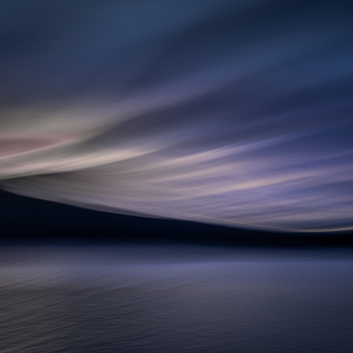 A blurry, abstract photo of a dark lake under a dramatic sky with streaks of blue and purple, suggesting motion and a tranquil, moody atmosphere.