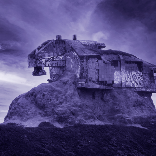 A weathered, graffiti-covered concrete bunker sits atop a craggy hill against a cloudy, purple-tinted sky.