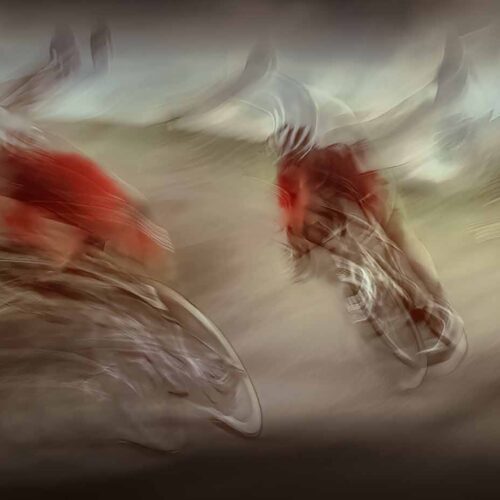 three cyclists in red jerseys ride at high speed, creating a motion blur effect that gives the image an abstract and dynamic appearance. the background and surroundings are also blurred, emphasizing their rapid movement.