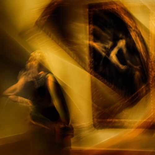 abstract, blurry image with warm yellow and brown tones, showing a figure in motion beside a tilted, framed artwork. the scene appears dreamlike and surreal due to the motion blur and lighting effects.
